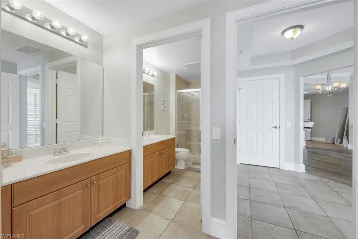 Full bath with two vanities, a shower stall, a chandelier, tile patterned flooring, and baseboards