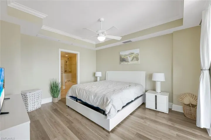 Bedroom featuring a tray ceiling, light wood-style flooring, baseboards, and crown molding