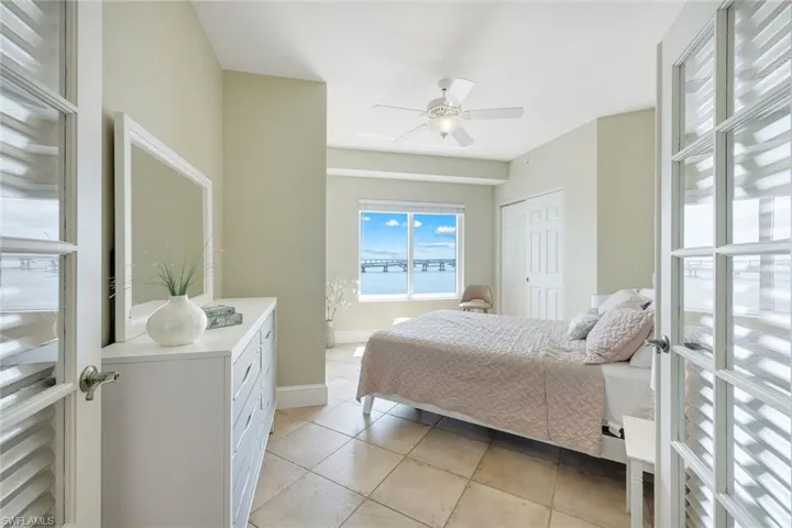 Bedroom with light tile patterned flooring, a water view, a closet, a ceiling fan, and baseboards