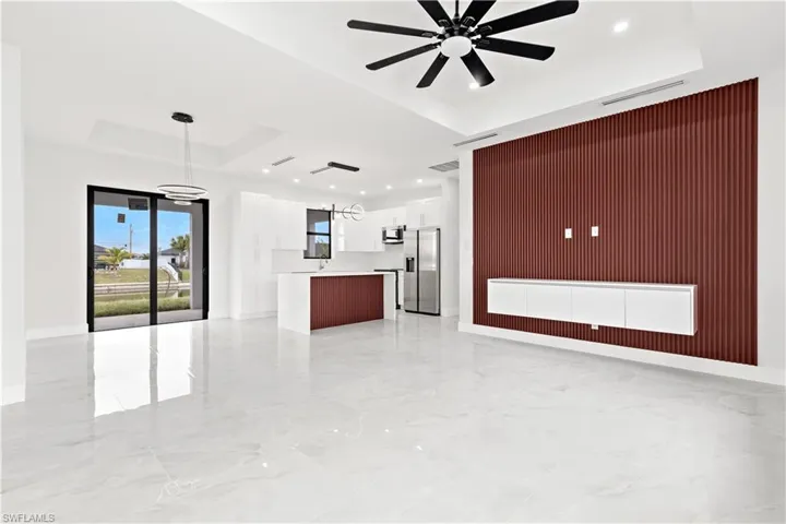 Unfurnished living room with ceiling fan with notable chandelier, a raised ceiling, and wooden walls