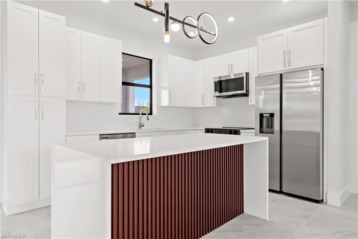 Kitchen featuring appliances with stainless steel finishes, decorative light fixtures, a kitchen island, and white cabinetry
