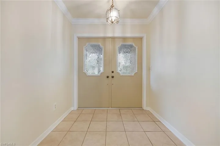 Doorway to outside with ornamental molding, light tile patterned flooring, a notable chandelier, and french doors