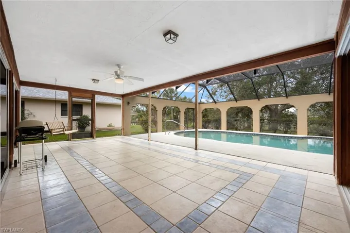 View of pool with ceiling fan, grilling area, glass enclosure, and a patio