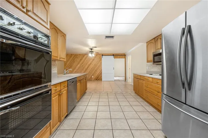 Kitchen with light tile patterned floors, ceiling fan, appliances with stainless steel finishes, backsplash, and wood walls