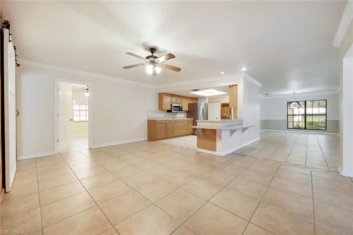 Kitchen featuring a breakfast bar, stainless steel appliances, ornamental molding, a barn door, and kitchen peninsula
