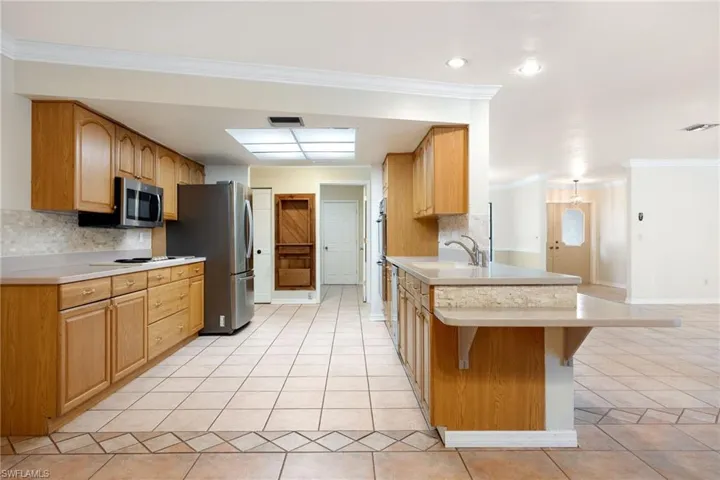 Kitchen featuring ornamental molding, a breakfast bar area, stainless steel appliances, and light tile patterned flooring