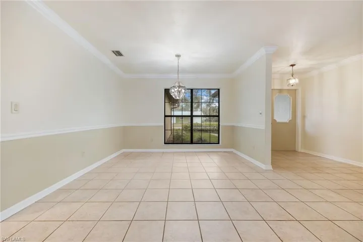 Tiled empty room featuring crown molding and an inviting chandelier