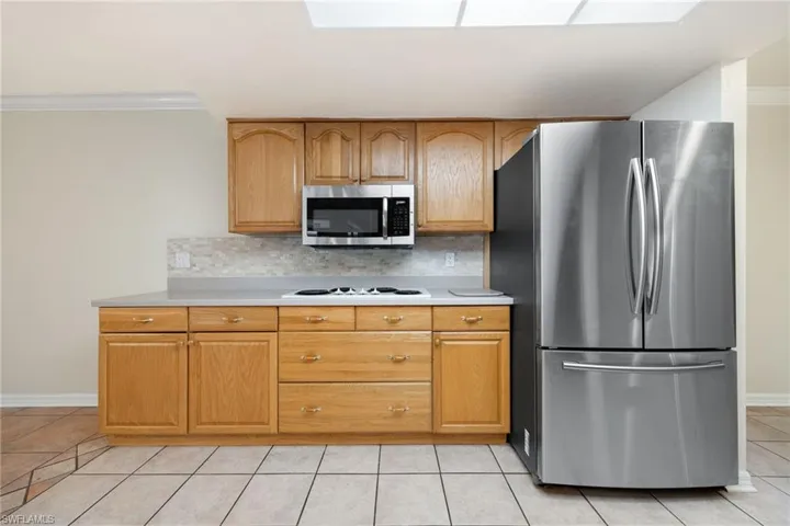 Kitchen with stainless steel appliances, a skylight, light tile patterned floors, and backsplash