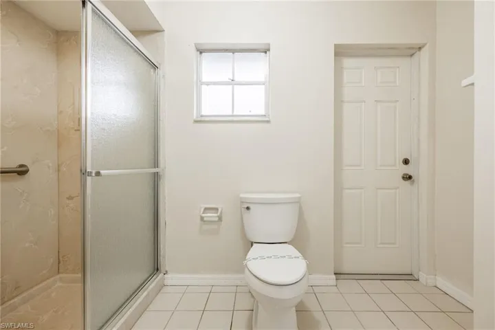 Bathroom with a shower with door, tile patterned floors, and toilet