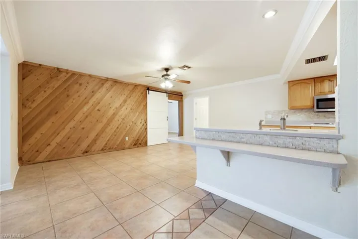 Kitchen featuring a breakfast bar, wood walls, ornamental molding, a barn door, and decorative backsplash