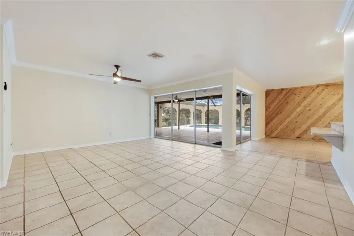 Tiled empty room featuring ceiling fan, ornamental molding, and wooden walls