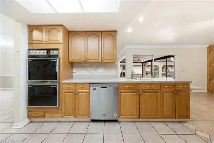 Kitchen featuring dishwasher, multiple ovens, light tile patterned floors, and crown molding