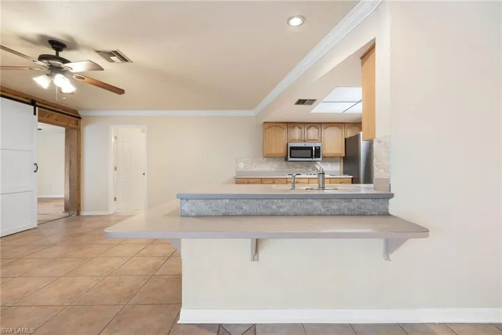 Kitchen featuring appliances with stainless steel finishes, a kitchen bar, kitchen peninsula, a barn door, and light brown cabinets