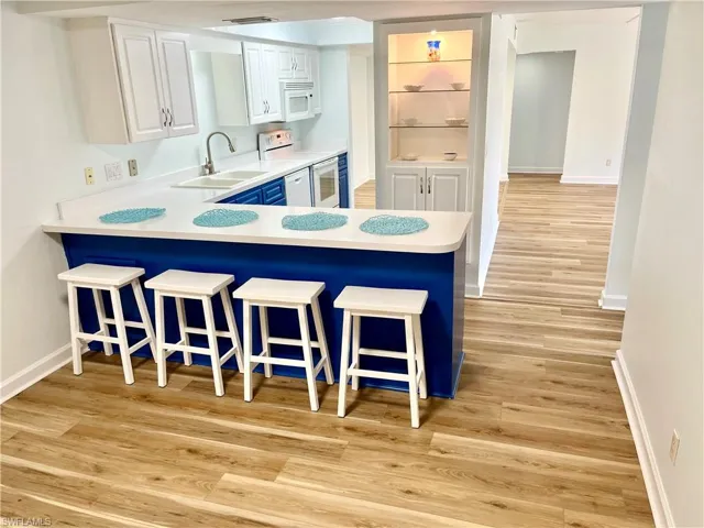 Kitchen with light hardwood / wood-style flooring, white cabinets, a kitchen bar, and white appliances