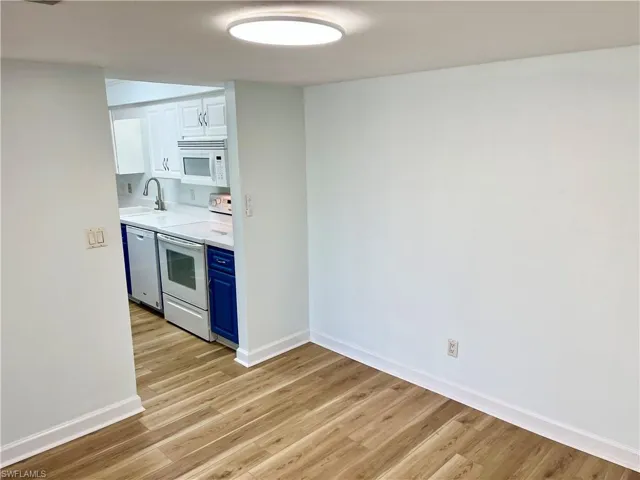 Kitchen with blue cabinetry, sink, light wood-type flooring, and white appliances
