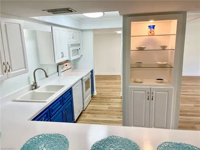 Kitchen with light hardwood / wood-style flooring, sink, blue cabinets, white cabinets, and white appliances