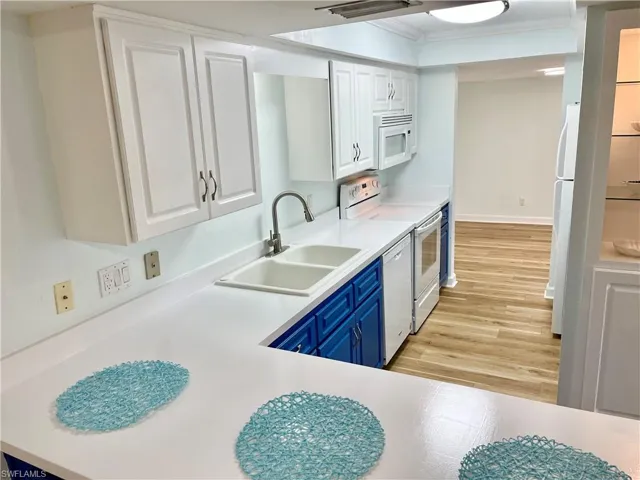 Kitchen with white cabinetry, light wood-type flooring, sink, blue cabinets, and white appliances