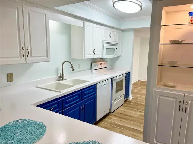 Kitchen with white appliances, sink, white cabinets, ornamental molding, and light hardwood / wood-style flooring