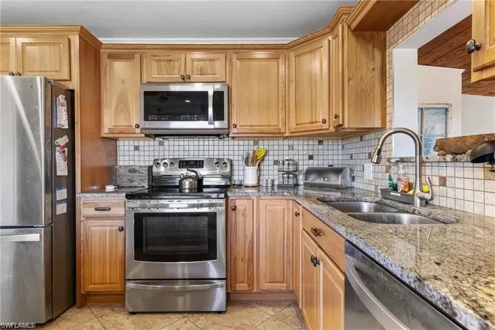 Kitchen with stainless steel appliances, light tile floor, Granite counters, dble sink and tasteful backsplash