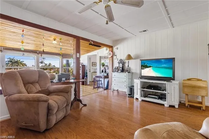 Living room featuring hardwood / wood-style floors, ceiling fan, wooden walls, and lofted ceiling
