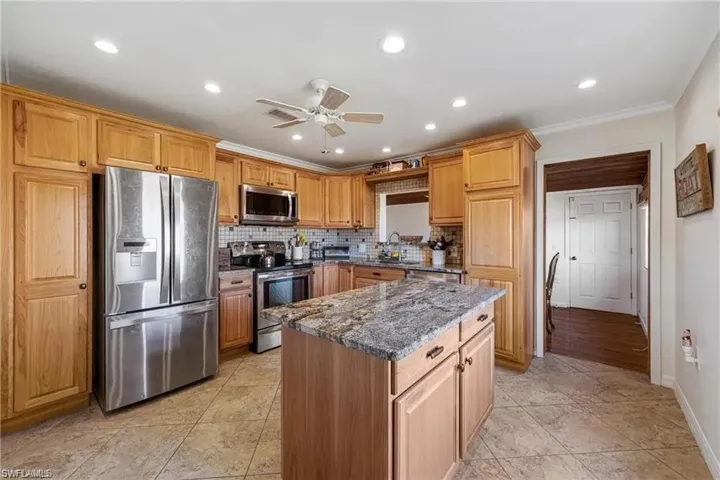 Kitchen featuring wood cabs, granite counters, St St appliances, decorative backsplash, and a center island
