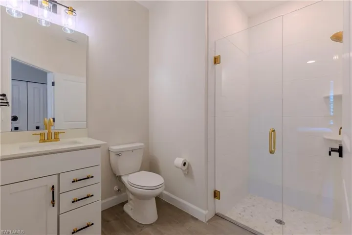 Bathroom with baseboards, toilet, vanity, wood finished floors, and a stall shower