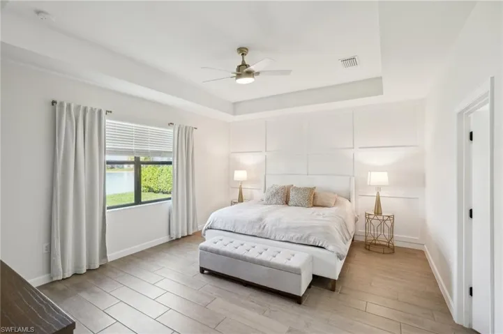 Bedroom featuring baseboards, light wood-style flooring, visible vents, a tray ceiling, and a decorative wall