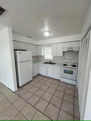 Kitchen featuring light countertops, white appliances, tasteful backsplash, and white cabinets