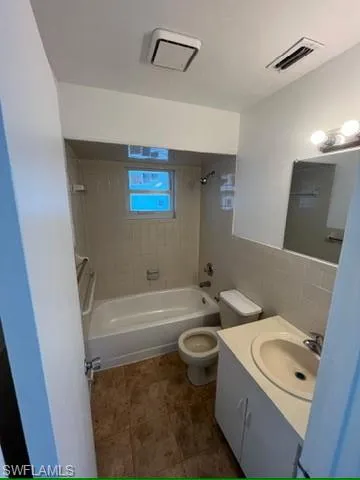 Full bath with shower / bath combination, vanity, and tile walls