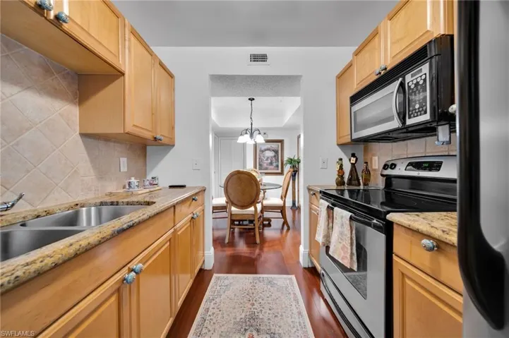 Kitchen with stainless steel range with electric cooktop, black microwave, suspended lighting, light stone counters, and fridge