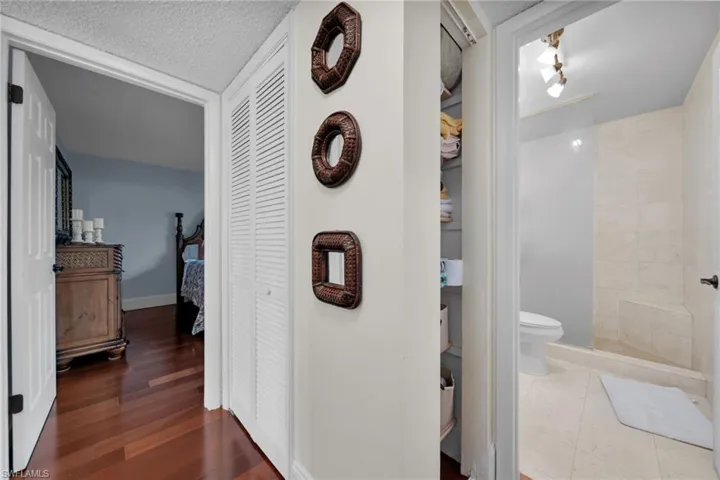 Bathroom featuring a closet, a textured ceiling, a tile shower, and dark wood-style flooring