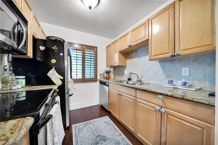 Kitchen featuring stainless steel appliances, light stone counters, light wood finish cabinetry, dark wood finished floors, and backsplash