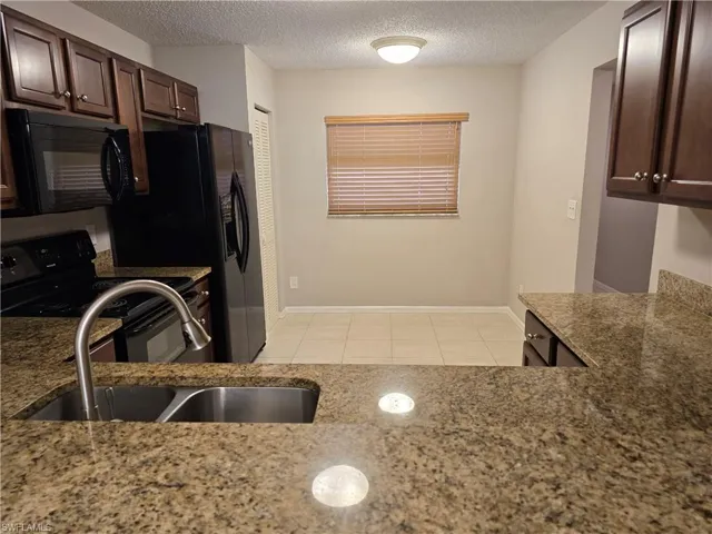 Kitchen featuring a textured ceiling, black appliances, light stone counters, dark brown cabinetry, and light tile patterned floors