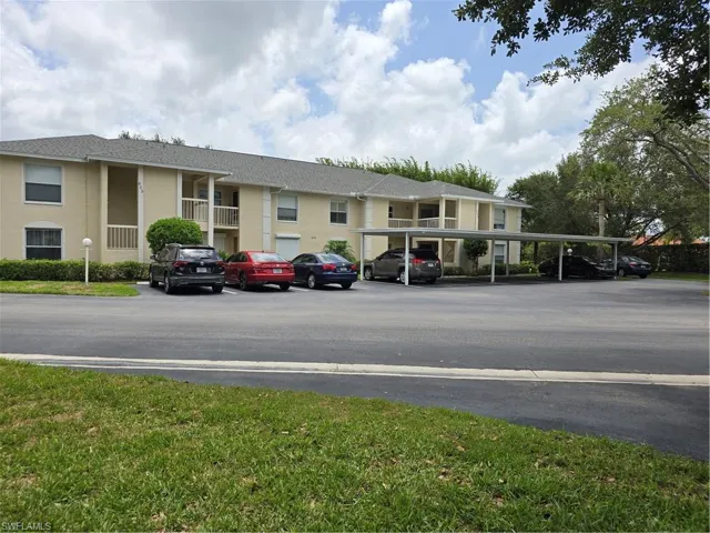 View of building exterior featuring covered and uncovered parking