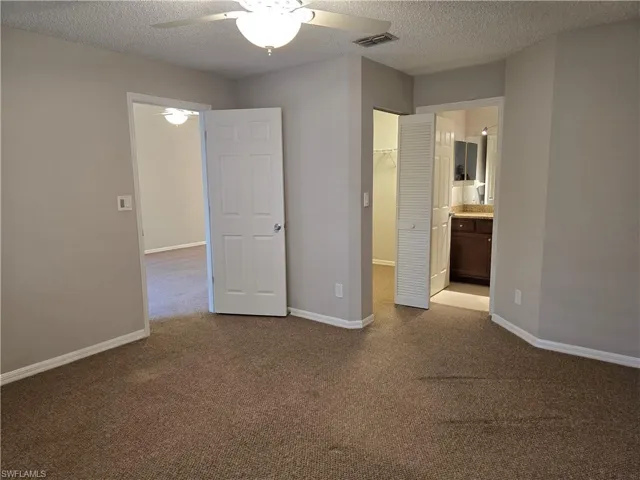 Master bedroom with a textured ceiling, carpet flooring, a walk-in closet, ensuite bathroom, and a ceiling fan