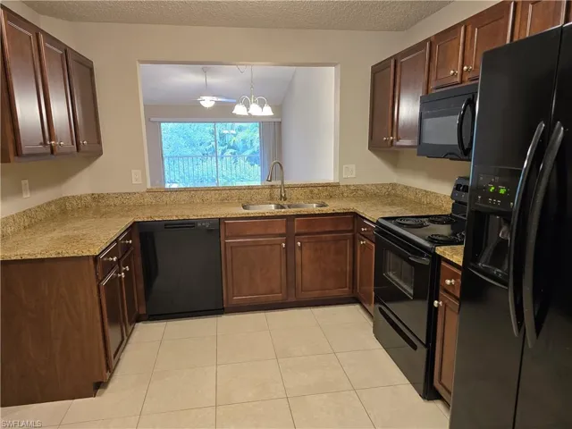 Kitchen featuring black appliances, light tile patterned floors, a textured ceiling, and light stone counters