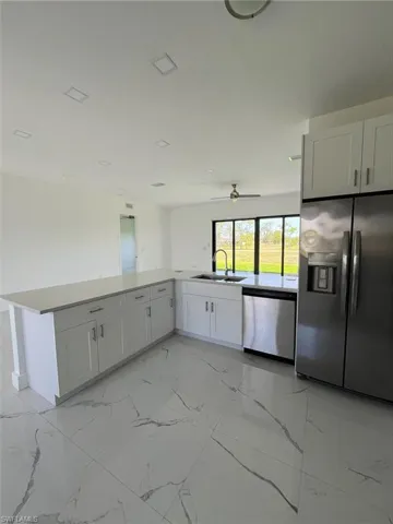 Kitchen featuring light marble finish flooring, appliances with stainless steel finishes, white cabinetry, and light stone counters
