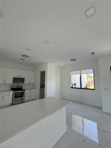 Kitchen with light marble finish flooring, white cabinets, appliances with stainless steel finishes, and light stone counters