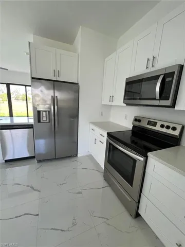 Kitchen featuring appliances with stainless steel finishes, light marble finish flooring, white cabinetry, and light stone countertops