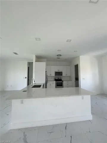 Kitchen with light marble finish flooring, white cabinets, stainless steel appliances, light stone countertops, and open floor plan