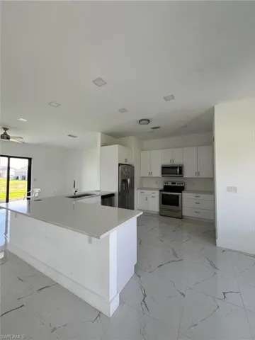 Kitchen with light marble finish flooring, appliances with stainless steel finishes, white cabinets, and a peninsula