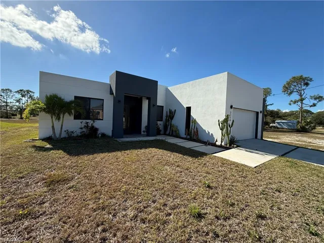 View of front of house with stucco siding, a front yard, driveway, and a garage