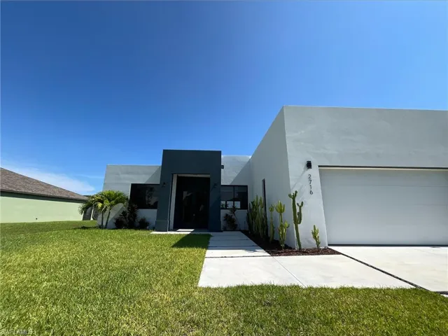 Contemporary home featuring a front lawn, stucco siding, a garage, and driveway