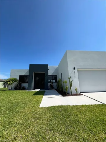 Contemporary house with a front yard, stucco siding, a garage, and concrete driveway