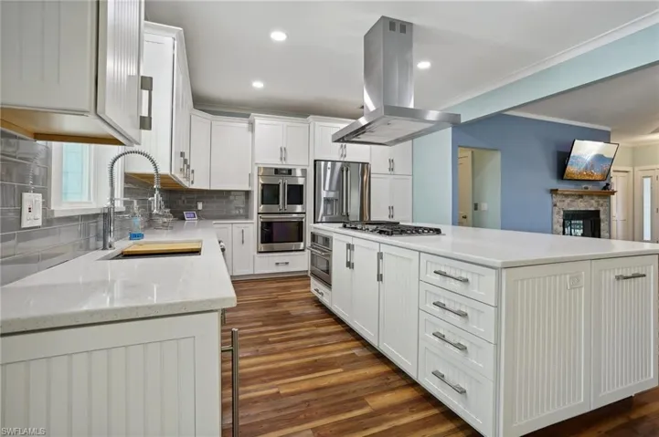 Kitchen featuring a fireplace, white cabinets, island exhaust hood, appliances with stainless steel finishes, and dark wood-type flooring