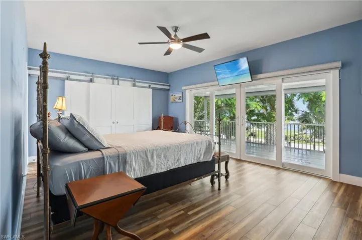Bedroom featuring access to exterior, ceiling fan, wood-type flooring, and a barn door