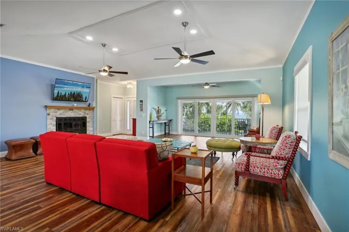 Living room featuring ceiling fan, lofted ceiling, a stone fireplace, and dark wood-type flooring