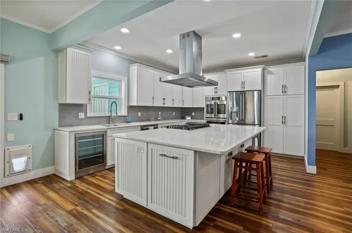 Kitchen featuring island range hood, sink, a center island, dark wood-type flooring, and wine cooler