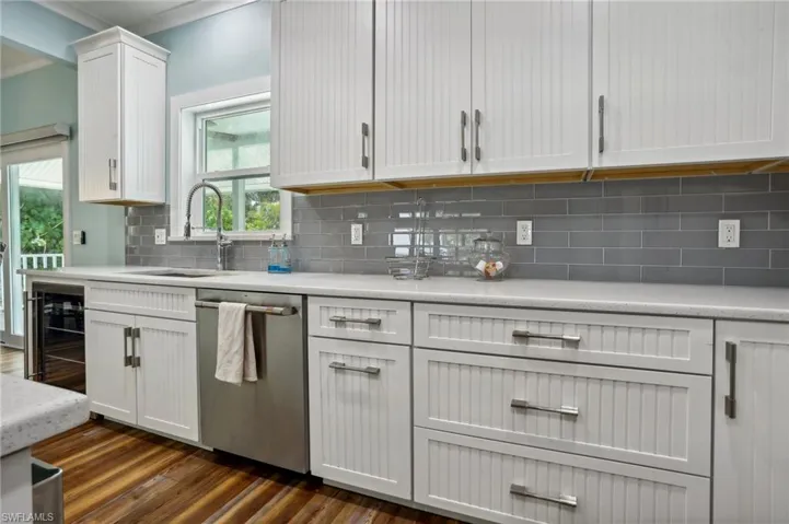 Kitchen with white cabinetry, tasteful backsplash, stainless steel dishwasher, dark hardwood / wood-style floors, and sink