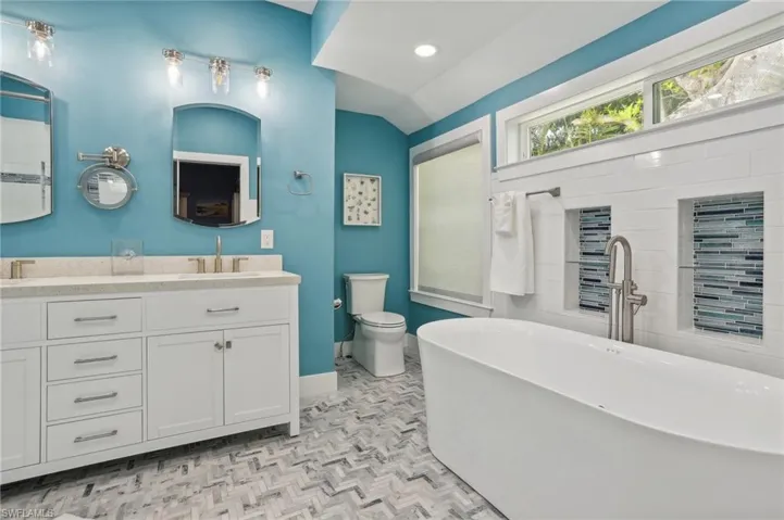 Bathroom featuring parquet floors, a tub, dual bowl vanity, toilet, and lofted ceiling